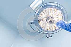 Doctor or surgeon in blue gown holding surgical lamp to adjust light inside operating theatre with space in background.