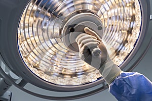 Doctor or surgeon in blue gown holding surgical lamp to adjust light inside operating theatre with space in background.