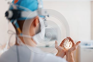 Doctor surgeon in medical mask in professional magnifying glasses shines on his hand with a flashlight, preparing for surgery.