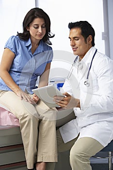 Doctor In Surgery With Female Patient Discussing Notes On Digital Tablet