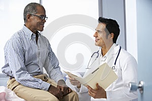 Doctor In Surgery With Male Patient Reading Notes