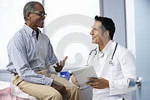 Doctor In Surgery With Male Patient Using Digital Tablet