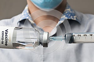 Doctor with surgical mask fills a syringe with the covid-19 vaccine to inject it