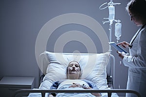 Doctor with tablet next to bed with dying elderly woman with can