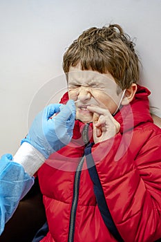 Doctor tacking a coronavirus test to an elementary age boy\'s nose with a medical swab. Respiratory virus testing procedure
