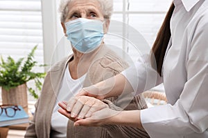 Doctor taking care of senior woman with mask at nursing home, focus on hands