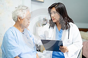 Doctor talking about diagnosis and note on clipboard with Asian senior or elderly old lady woman while lying on bed in nursing