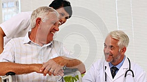 Doctor talking with elderly patient in a wheelchair being pushed by nurse