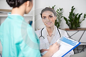 Doctor talking with internist writing in clipboard with diagnosis in clinic photo