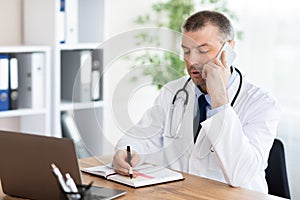 Doctor talking on phone with patient and writing notes