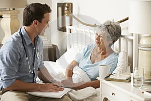 Doctor Talking With Senior Female Patient In Bed At Home