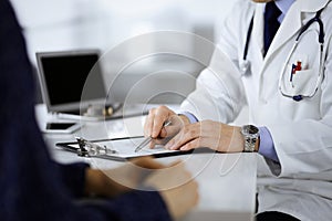 A doctor is talking to his patient, while sitting together at the desk in the cabinet in a hospital. Physician using