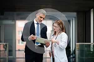 Doctor talking to pharmaceutical sales representative, presenting new medication. Hospital manager talking with female