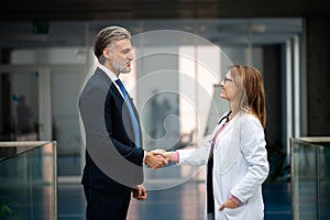 Doctor talking to pharmaceutical sales representative, shaking hands. Hospital manager talking with female doctor. Side