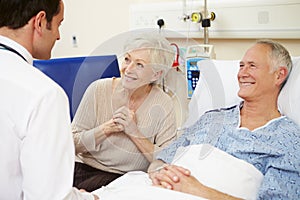 Doctor Talking To Senior Couple By Hospital Bed