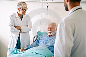 Doctor talking to senior male patient in hospital bed who is recovering from the disease