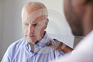 Doctor Talking To Unhappy Male Patient In Exam Room