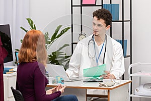 A doctor talks to a redheaded patient with a smile on his face. An adult woman in a doctor's office