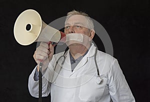 Doctor with tape across his mouth trying to shout into a megaphone photo