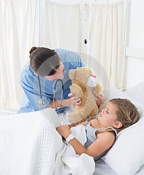 Doctor with teddy bear entertaining sick girl