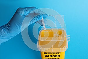 Doctor throwing used syringe needle into sharps container on light blue background, closeup