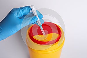 Doctor throwing used syringe into sharps container on white background, closeup