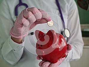 Doctor throws coin with red pig into piggy bank