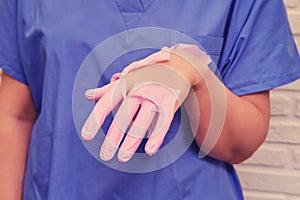 Doctor in a torn pink medical glove, closeup. Hand nurse in a blue uniform shows a torn protective glove