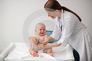 Doctor with a toy leaning towards an frightened newborn patient