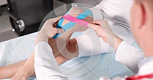 Doctor traumatologist glueing medical tapes on sore knee of woman patient 4k movie