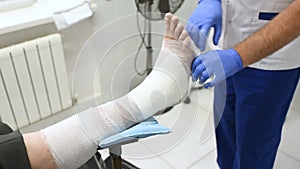 Doctor traumatologist puts a plaster on the broken leg of the patient.