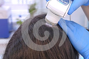 Doctor trichologist examines woman patient`s hairs using dermatoscope in clinic.