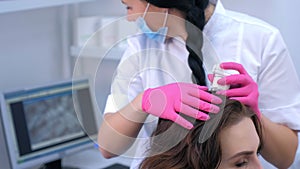 Doctor trichologist examines woman patient`s hairs using trichoscope in clinic.