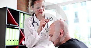 Doctor trichologist with magnifying glass examines bald head of man in clinic