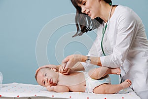 Doctor turning baby on side to exam with stethoscope on special table over blue
