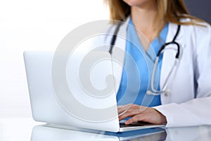 Doctor typing on laptop computer while sitting at the glass desk in hospital office. Physician at work. Medicine and