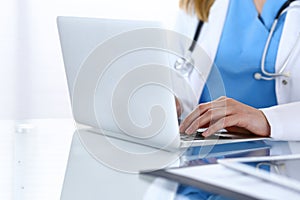 Doctor typing on laptop computer while sitting at the glass desk in hospital office. Physician at work. Medicine and