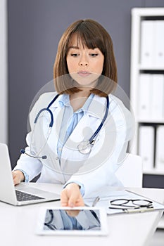 Doctor typing on laptop computer while sitting at the white table in hospital office. Physician at work. Medicine and