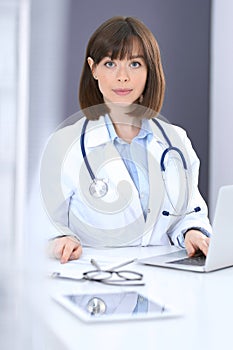 Doctor typing on laptop computer while sitting at the white table in hospital office. Physician at work. Medicine and