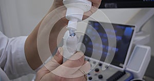 A doctor in uniform holds a transducer from an ultrasound machine in his hand and applies a gel to it to conduct a study