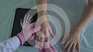 A doctor uses X-ray to examine a patients hand placed on examination table, while holding the hand with pink medical