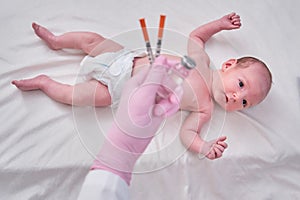 The doctor uses a syringe to inject a newborn child. A nurse in uniform is preparing to vaccinate a child