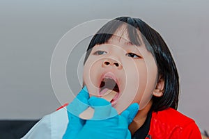 The doctor uses a tongue depressor to examine the child\'s tongue