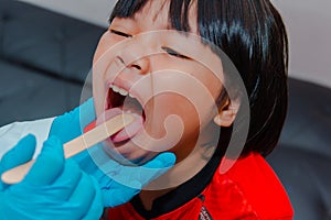 The doctor uses a tongue depressor to examine the child\'s tongue