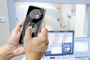 The doctor is using a cell phone to check the patient`s brain MRI results. The background is an electromagnetic control room.