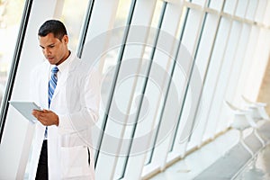 Doctor Using Digital Tablet In Corridor Of Modern Hospital