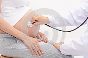 Doctor using hand and stethoscope while examining young pregnant woman in clinic,Medical exam concept