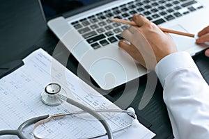 Doctor using laptop and stethoscope on healthcare report