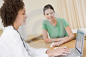 Doctor using laptop with woman in doctor's office