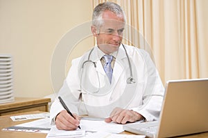 Doctor using laptop and writing in doctor's office